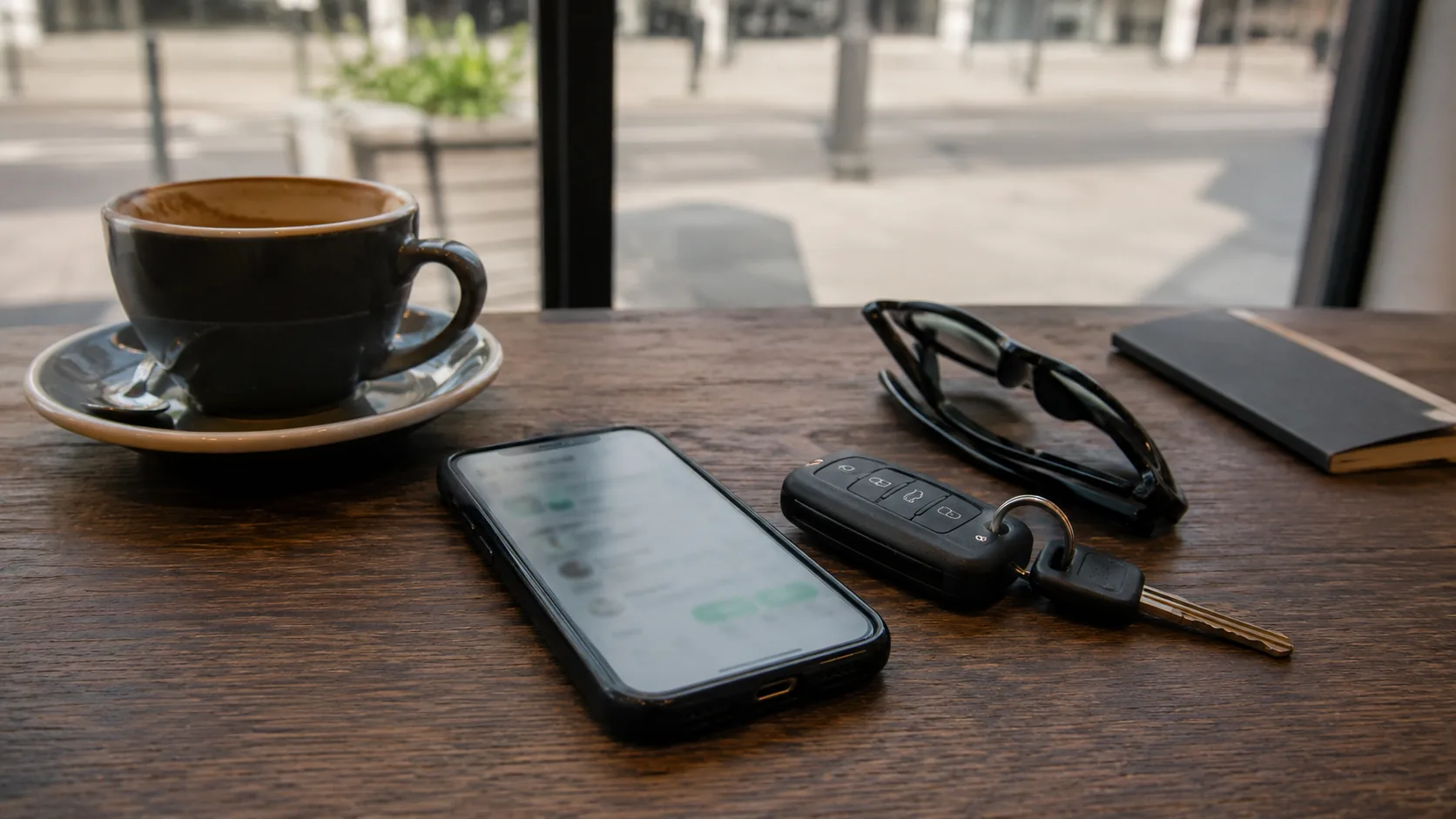 Telefon, kluczyk samochodowy, okulary i filiżanka kawy na stole